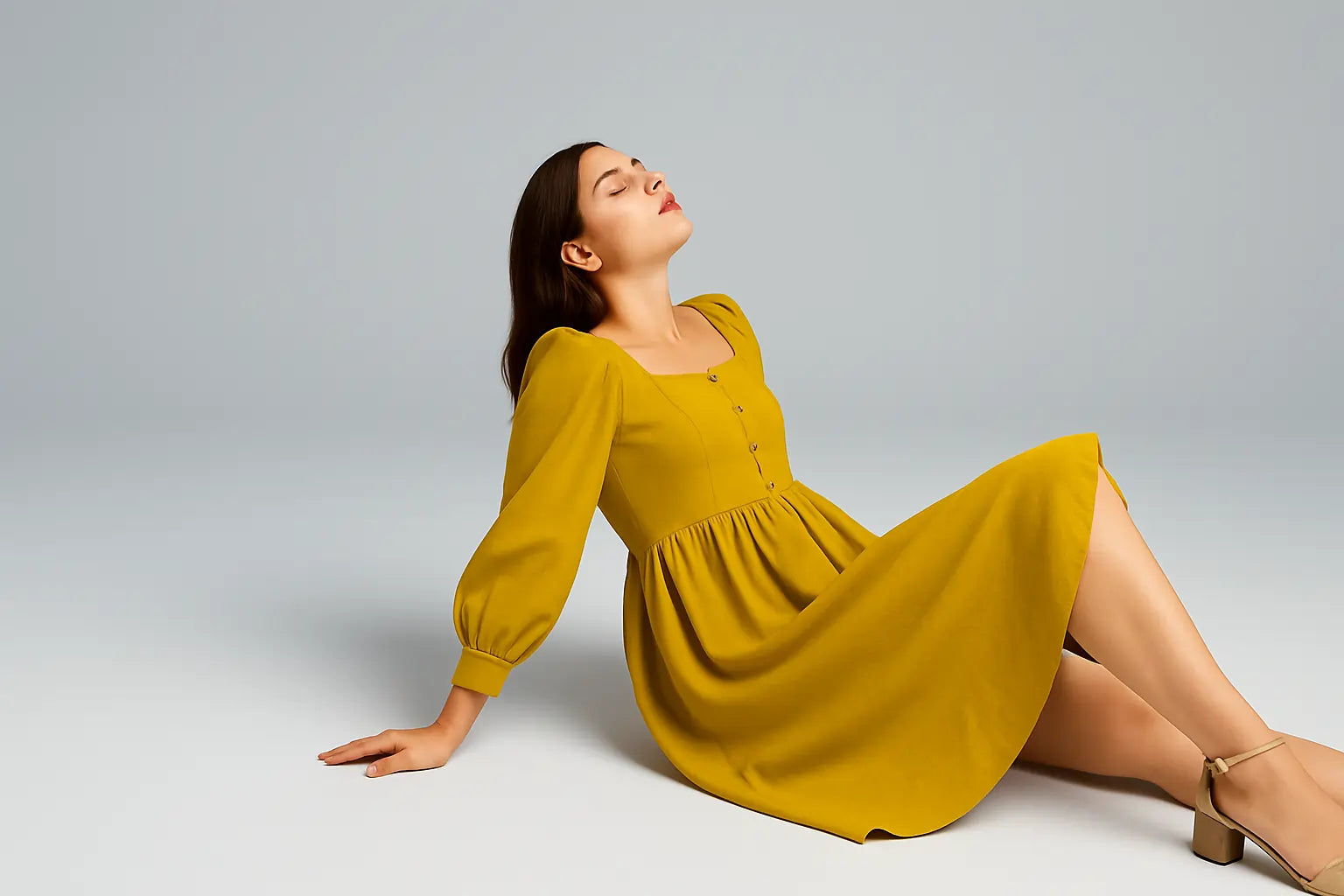 Woman in a yellow dress sitting on a gray background
